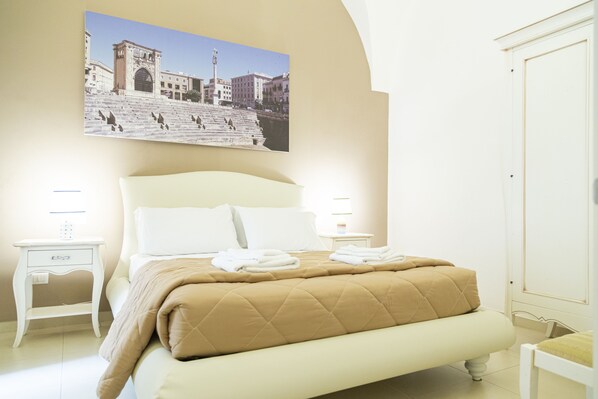 A bedroom with a large bed, two bedside tables, a nightstand, a wall-mounted picture, and a door. - Casa Mamma Elvira (Lecce)