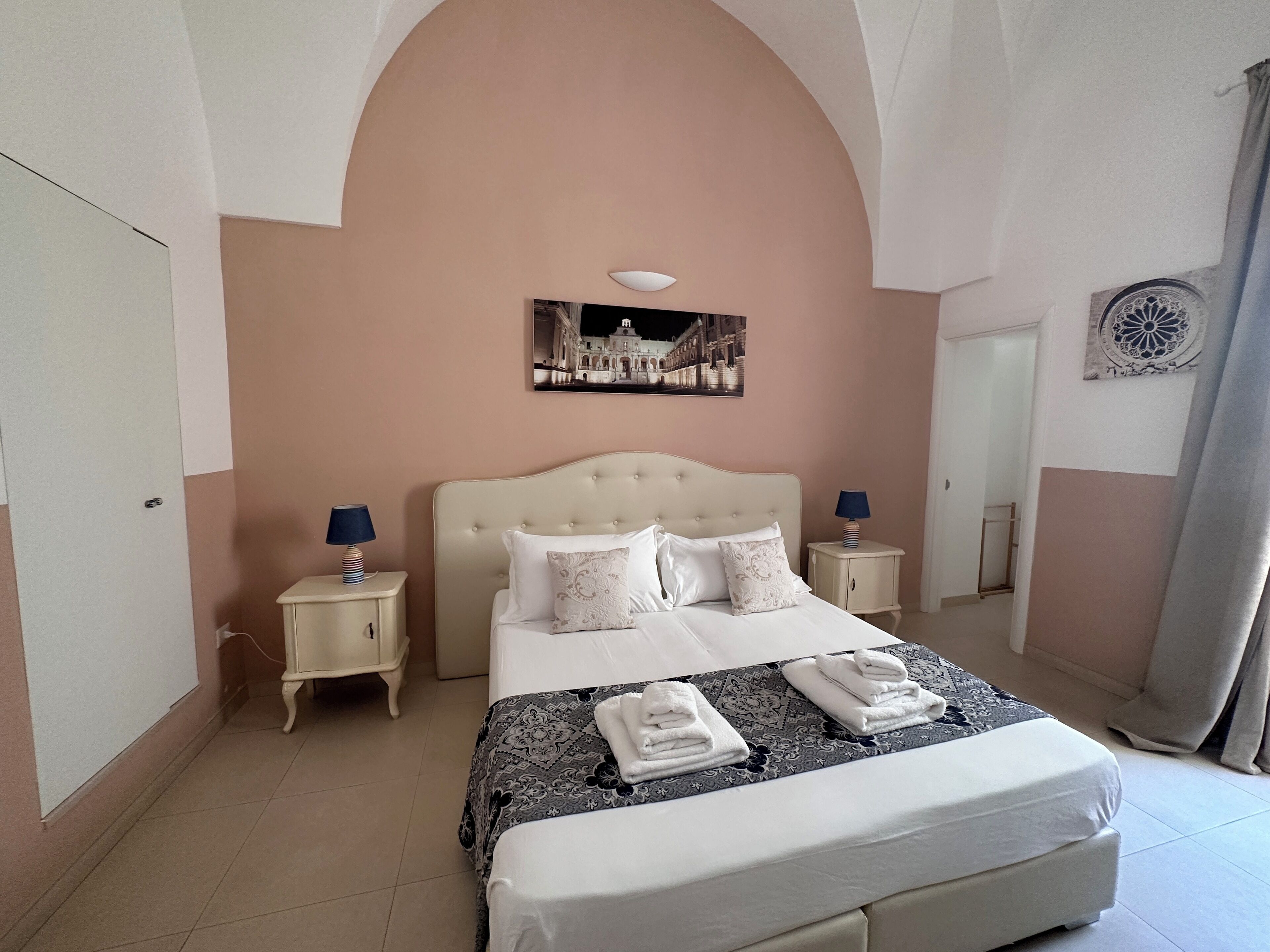 Un dormitorio con una cama grande, dos mesitas de noche, un cuadro en la pared y un espejo decorativo.