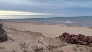 A beach with a rocky outcrop in the foreground and a calm sea under a cloudy sky. - HOT TUB,  BEACH 2 MINS, SEAFOOD, TRAILS, GOLF COURSES, DALVAY, DRIVE-IN THEATRE (York)