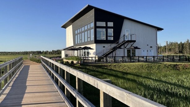 A modern building with a large window section, a wooden deck leading to it, and a staircase on the side. - HOT TUB,  BEACH 2 MINS, SEAFOOD, TRAILS, GOLF COURSES, DALVAY, DRIVE-IN THEATRE (York)
