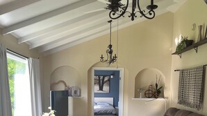 A cozy living room with a brown sofa, a wooden coffee table, and a chandelier. There is a doorway leading to a bedroom with a bed and a window. - HOT TUB,  BEACH 2 MINS, SEAFOOD, TRAILS, GOLF COURSES, DALVAY, DRIVE-IN THEATRE (York)