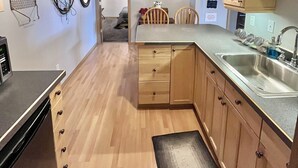 Una cucina compatta con mobili in legno, un lavello e un piano di lavoro. Sono presenti luci a sospensione e un piccolo tappeto sul pavimento.
