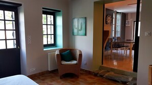 Une pièce avec un fauteuil en osier, une fenêtre, un radiateur et une vue sur un coin repas.