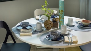 A dining table set with blue and white patterned dishes, a tall teal vase, and a view of greenery outside.
