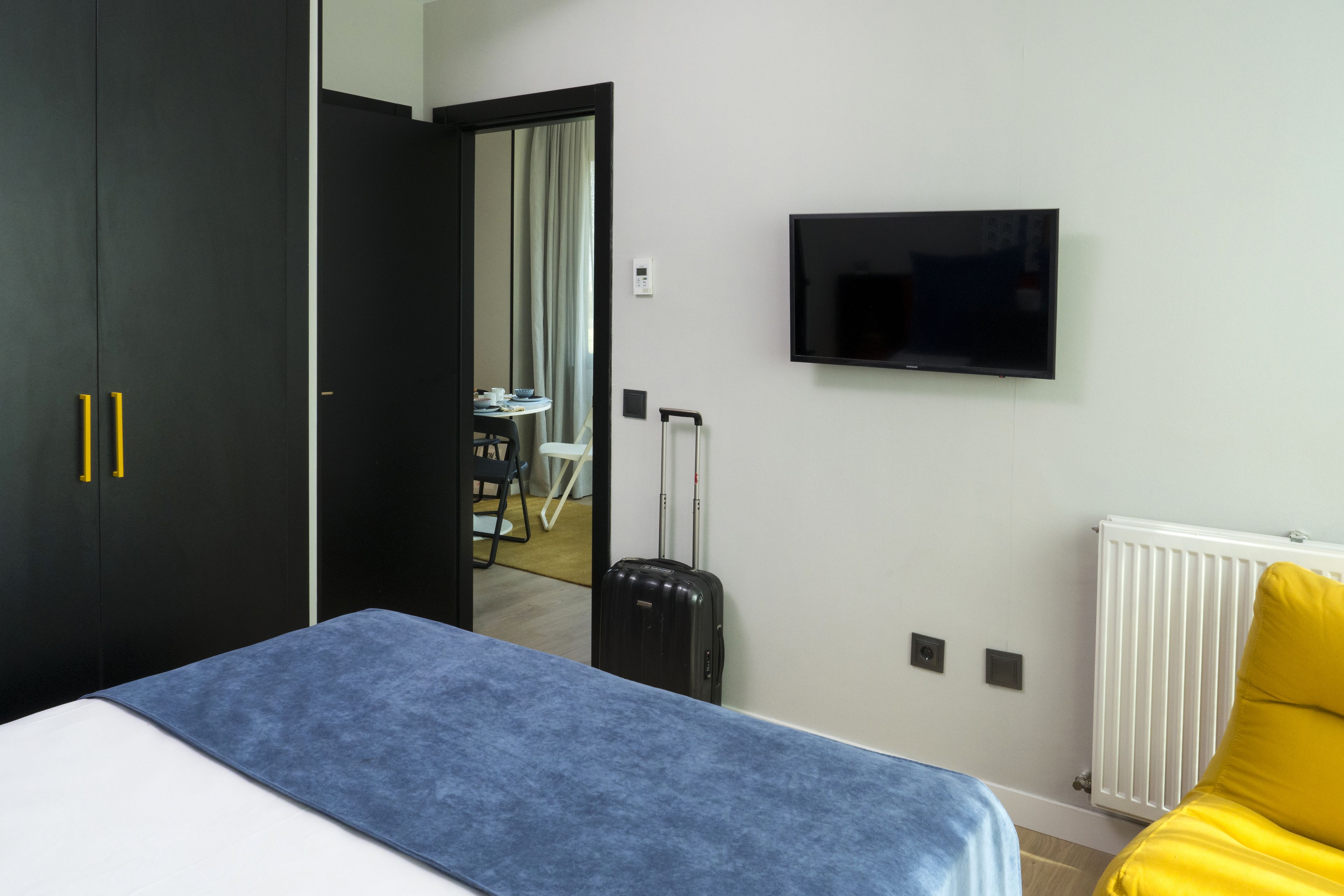 A hotel room with a bed, a television, a radiator, and a suitcase.