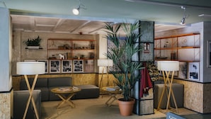A cozy living room with a sofa, two small tables, a large potted plant, and wooden shelving units.