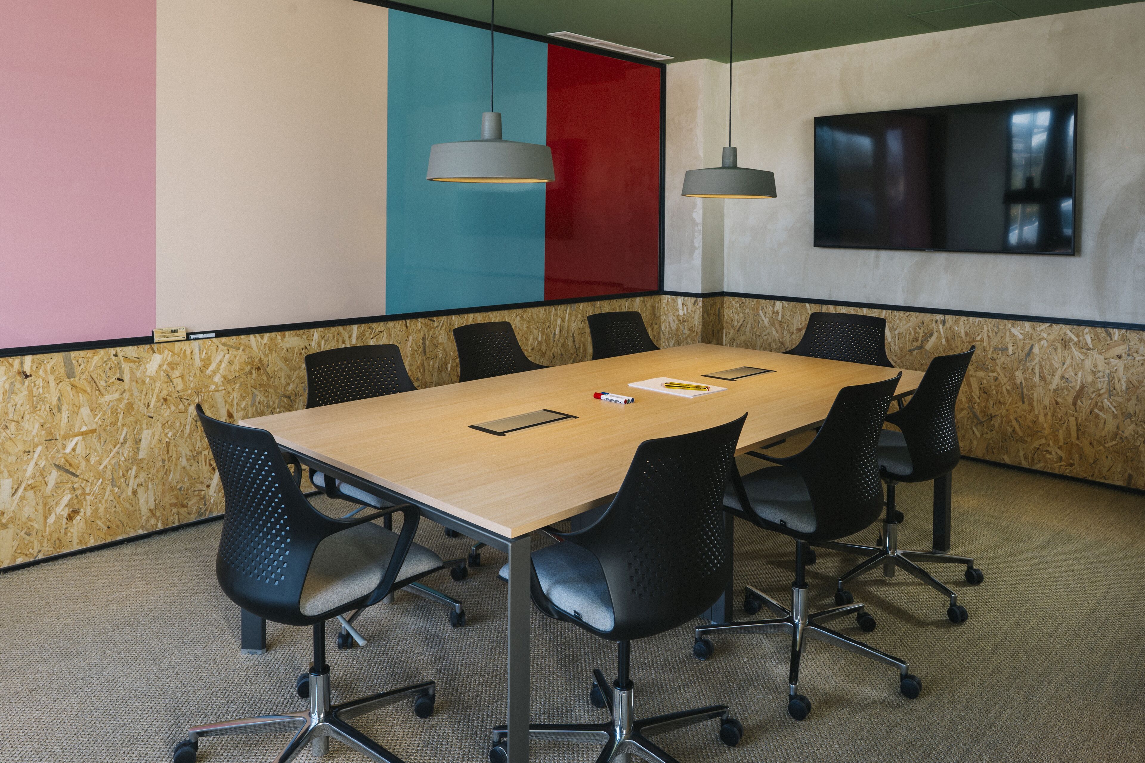 A conference room with a wooden table, black chairs, and a large flat-screen TV on the wall.