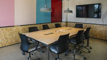 A conference room with a wooden table, black chairs, and a large flat-screen TV on the wall.