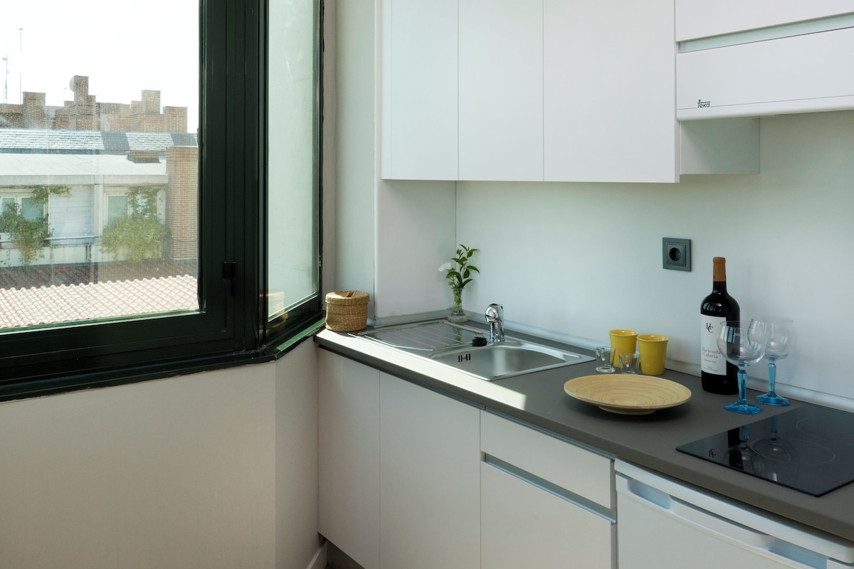 Una cocina moderna con ventana, pileta de acero inoxidable y una botella de vino.
