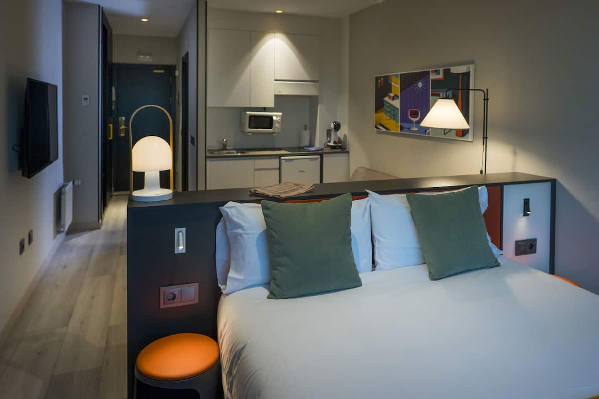 Ein Hotelzimmer mit Bett, Schreibtisch, Stuhl, Fernseher, Lampe, Mikrowelle, Spüle und einem Bild an der Wand.