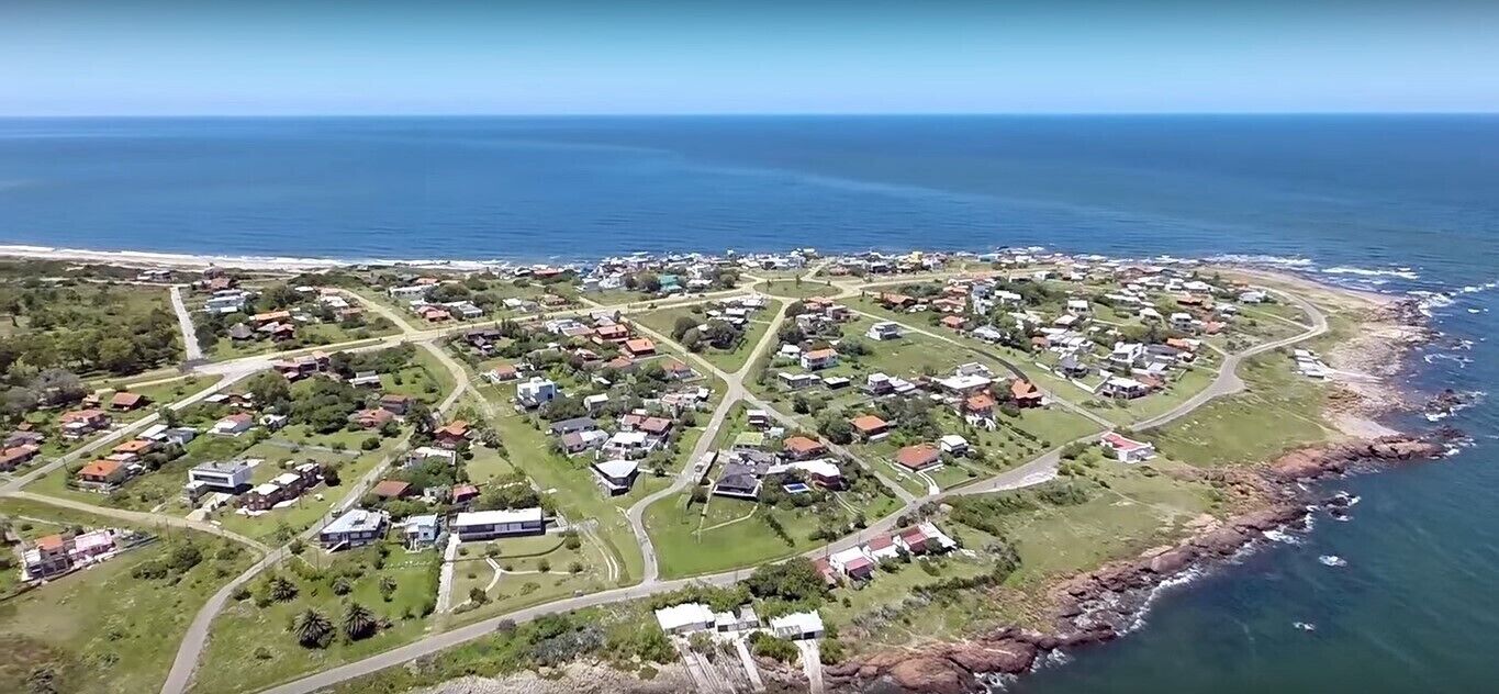 Vue aérienne d’une zone résidentielle côtière, avec des maisons, des routes et une plage.