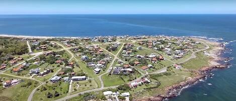 Vue aérienne d’une zone résidentielle côtière, avec des maisons, des routes et une plage.