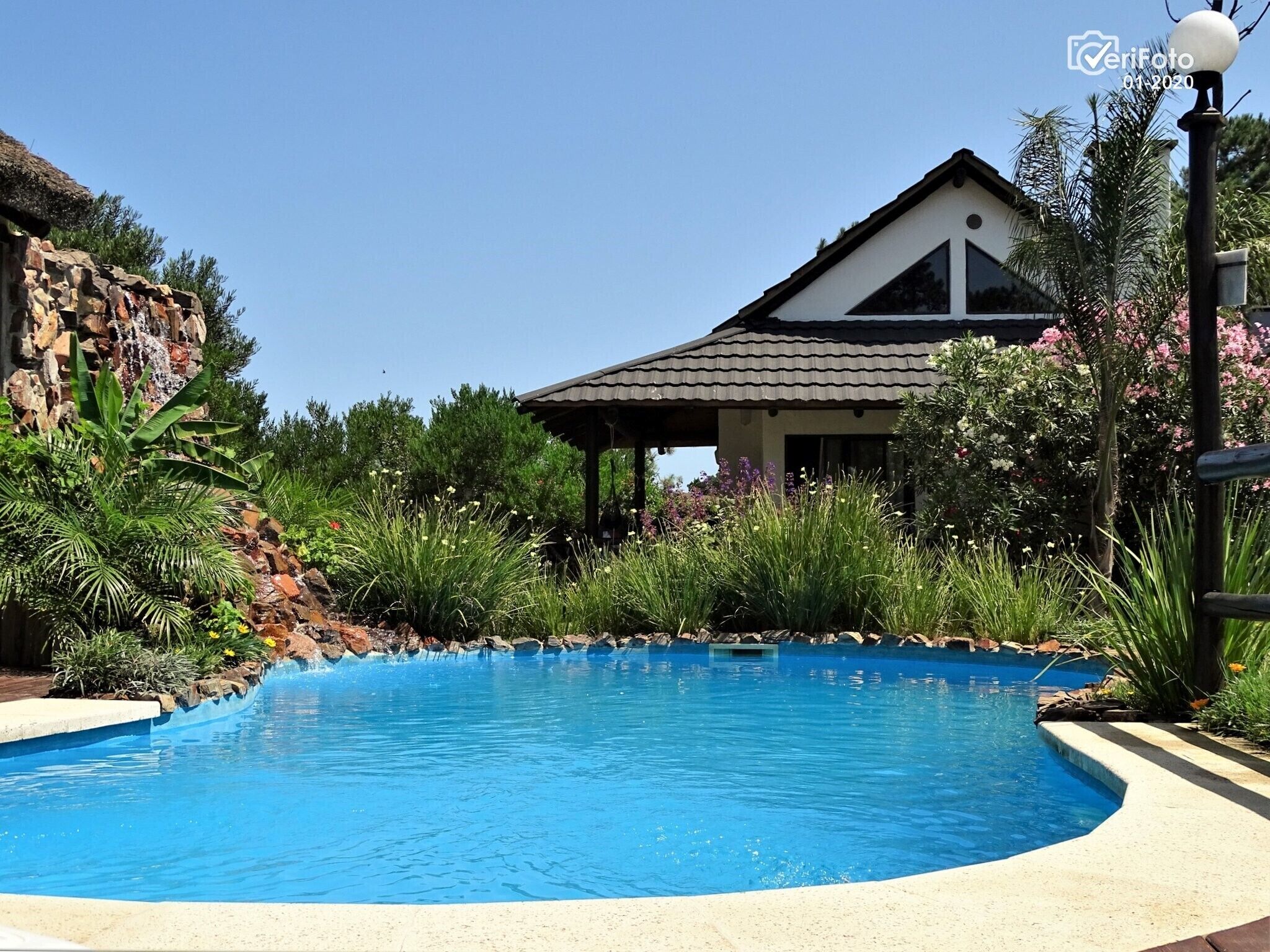 Una piscina con un muro de piedra y una casa al fondo.