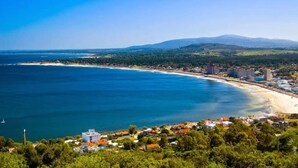 A coastal town with a beach, buildings, and a mountain in the background.