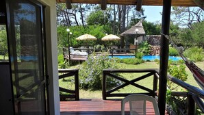 A wooden deck with a table and chairs, overlooking a pool area with umbrellas and lounge chairs.