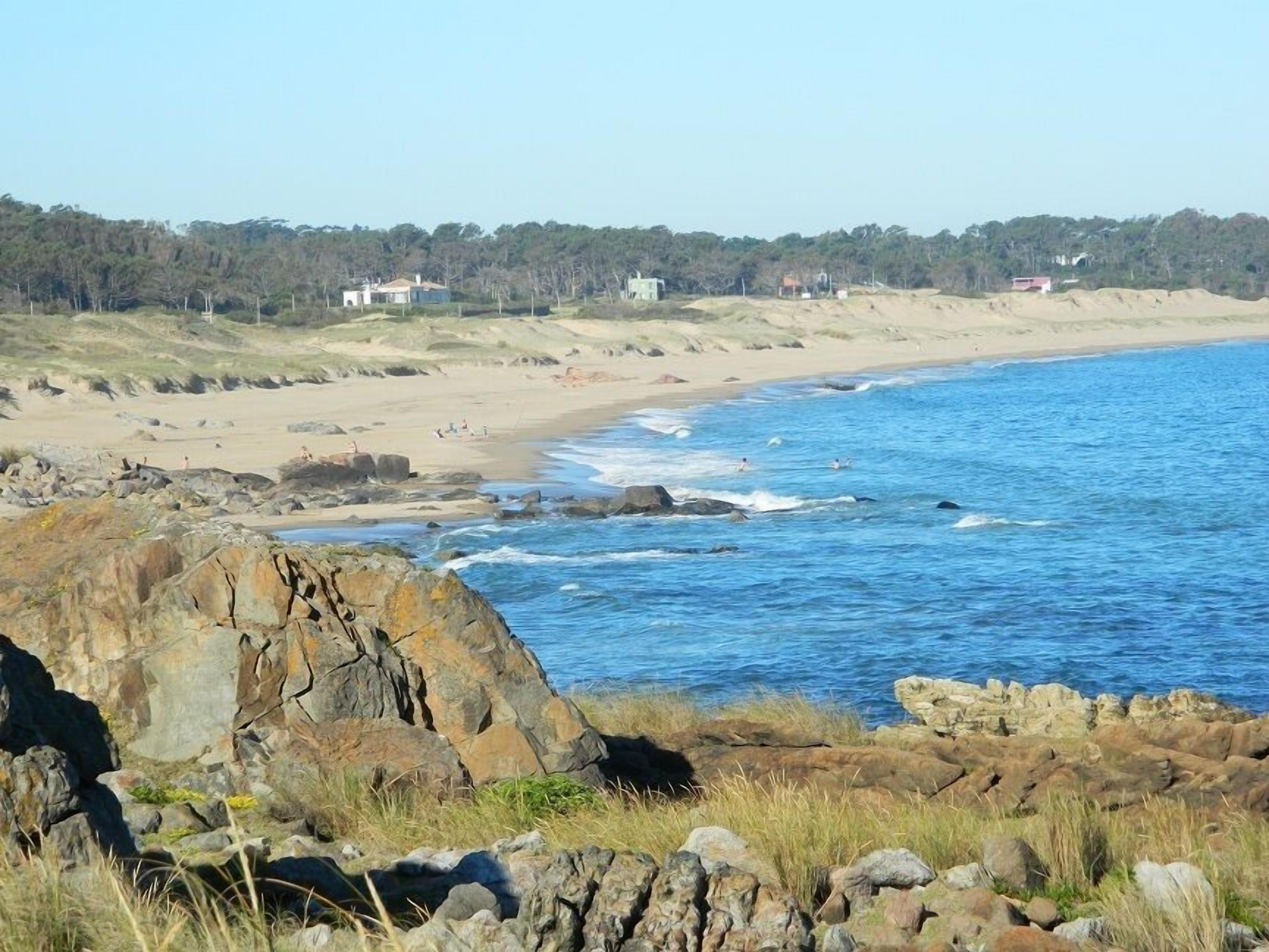 Un paisaje costero con afloramientos rocosos, una playa de arena y un mar azul claro.