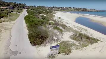 Una carretera costera con una playa a la derecha y casas al fondo.