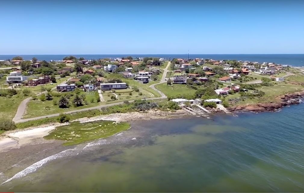 An aerial view of a coastal residential area with houses, roads, and a beach.