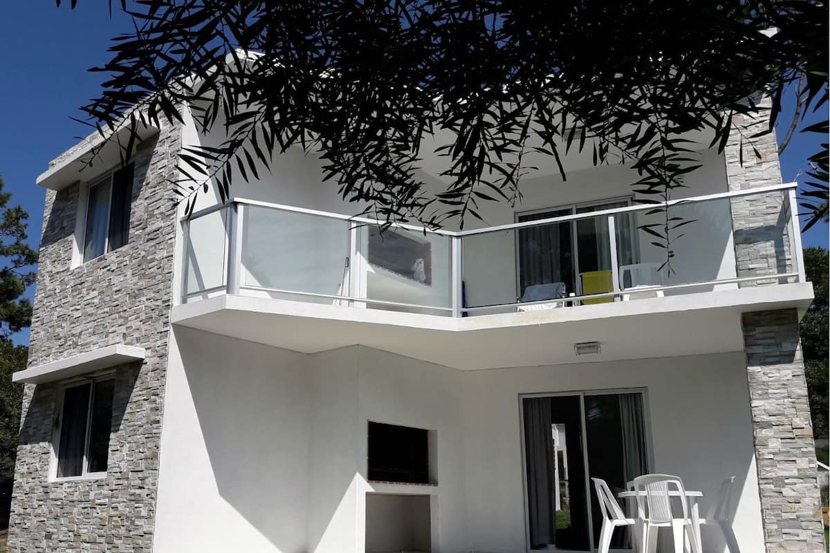 A two-story house with a balcony, stone facade, and a small patio area with a table and chairs.