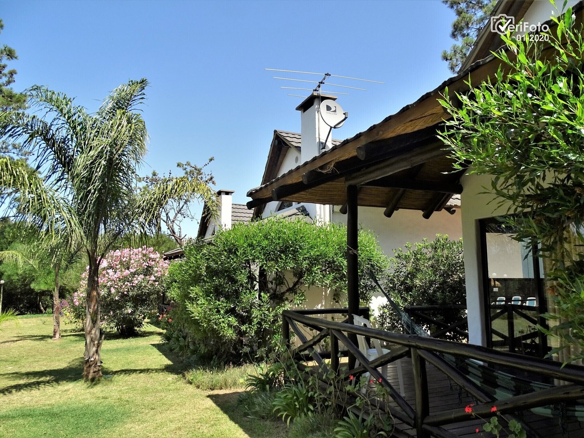 A garden with a wooden deck, a gazebo, and a building with a satellite dish.