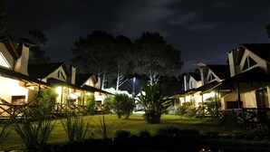 A row of two-story buildings with illuminated windows, surrounded by trees and a well-maintained lawn.