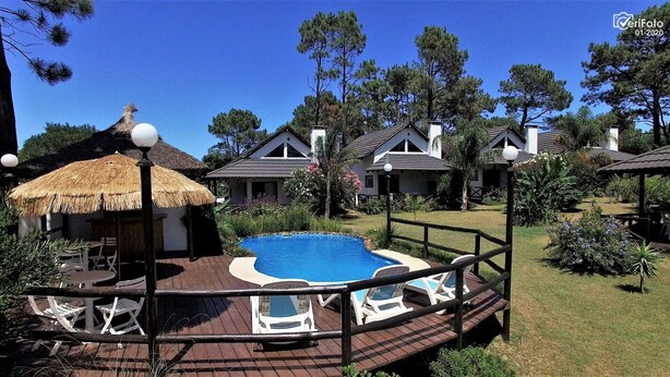 A pool area with a wooden deck, lounge chairs, and a thatched-roof structure.