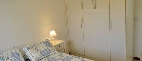 A bedroom with a bed, nightstand, lamp, wardrobe, and ceiling fan.