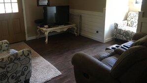 Ein Wohnzimmer mit Fernseher auf einem Schrank, einem gemusterten Sessel, einer Couch und einem dekorativen Teppich.