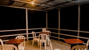 An outdoor seating area with white plastic chairs and wooden tables, under a metal roof structure. - Hotel Amoretto (Trujillo)