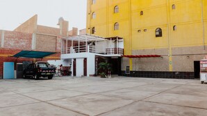 A parking area with a brick building and a yellow building in the background. - Hotel Amoretto (Trujillo)