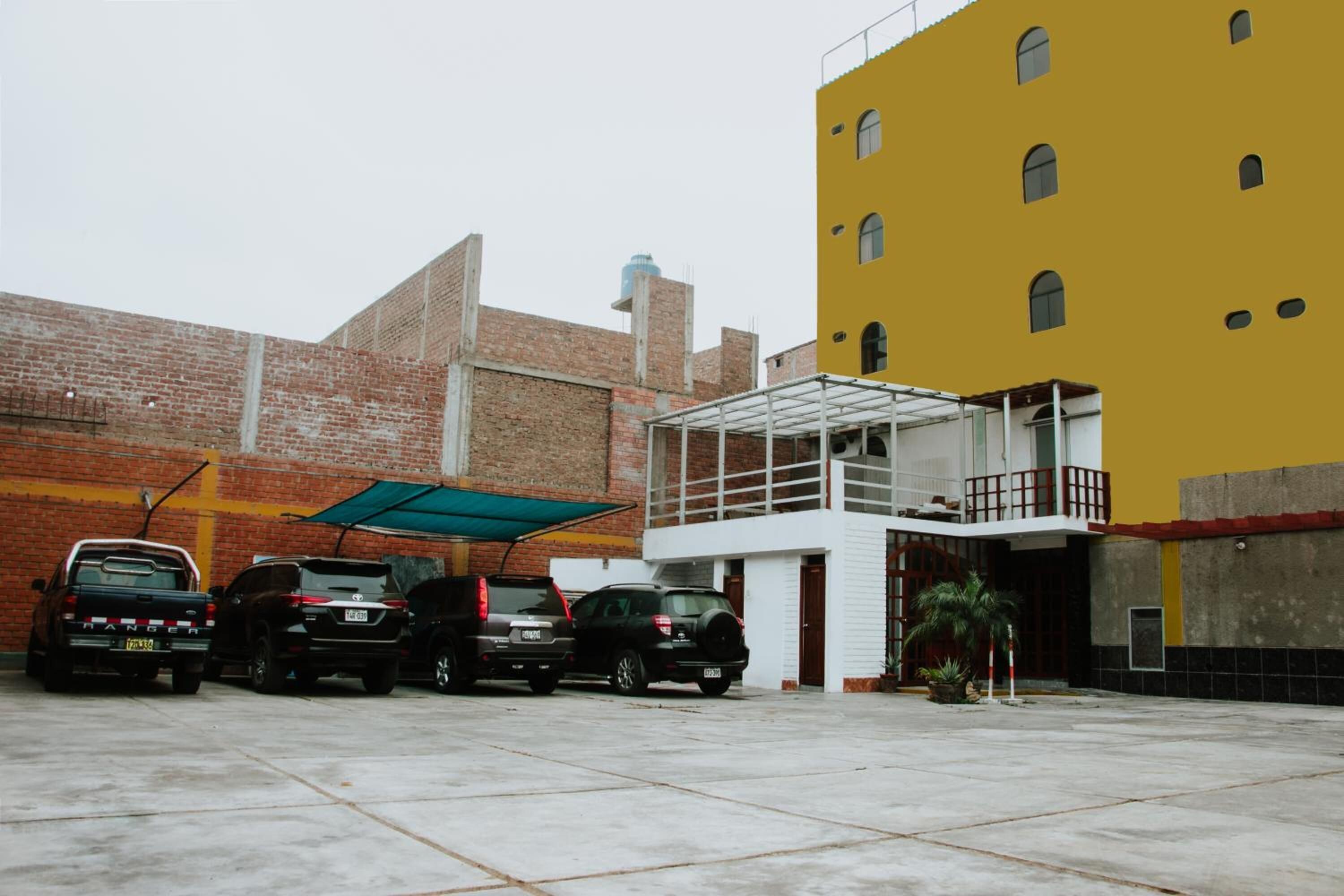 A parking area with four SUVs parked in a row, a yellow building with multiple windows, and a brick wall in the background.