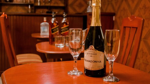 A bottle of Pramadonna wine on a wooden table with two empty wine glasses. - Hotel Amoretto (Trujillo)