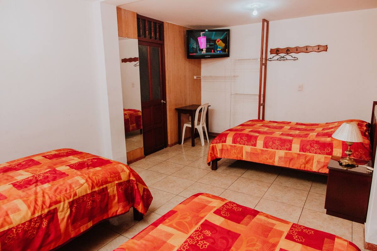 A bedroom with two beds, a television, a wooden door, and a small table.