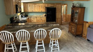 Een keuken met houten kastjes, een zwarte koelkast, een granieten aanrecht en een bar met witte stoelen.