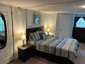 Een slaapkamer met een bed, nachtlampjes, een dressoir, een deur en een raam met gordijnen.