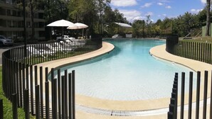 Une piscine au design incurvé, entourée d’une clôture et ombragée par des parasols.