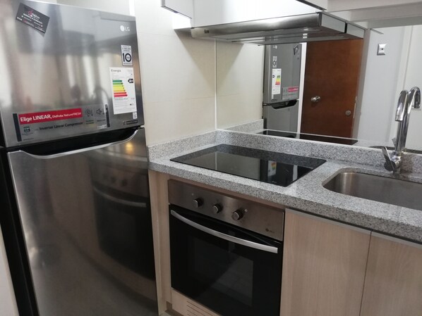 A kitchen with a stainless steel refrigerator, a built-in oven, a granite countertop, and a stainless steel sink.