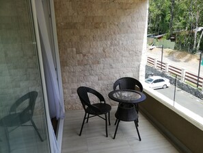 A balcony with two wicker chairs and a glass table, overlooking a street with cars and greenery. - Apartment near the center. New, very welcoming. (Pucon)