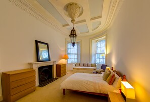 Classic bedroom with a large bed, dresser, and fireplace, offering a comfortable seating area and views of the outside.