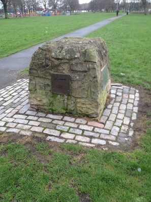 Situated in a park, this monument features a plaque surrounded by a brick border and a grassy area with a pathway.