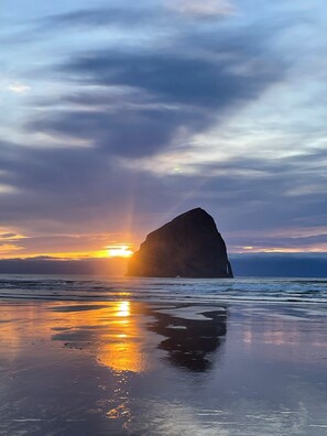 Una playa con una gran formación rocosa silueteada contra un atardecer.