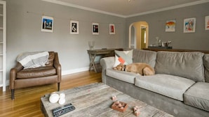 Ein Wohnzimmer mit braunem Ledersessel, grauem Sofa, Couchtisch aus Holz und Deckenventilator.