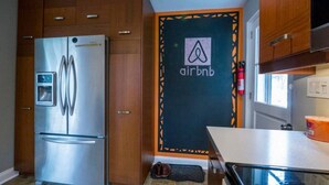 Eine kompakte Küche mit einem Edelstahl-Kühlschrank, Holzschränken und einer Tür mit dem Airbnb-Logo.
