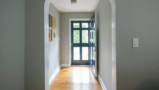 Ein Flur mit Holzboden, einer weißen Tür mit Glasfeldern und einem Lichtschalter an der Wand.