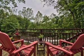 A wooden deck with two red Adirondack chairs and a small table with a potted plant. - Private 10-Acre Creekside Cabin—80-Ft Deck, Fire Pit, Wildlife & Cozy Spaces! (Canadensis)