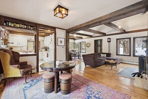 A spacious living area with a wooden floor, a round table with stools, a sofa, and a large window with a view of trees. - Private 10-Acre Creekside Cabin—80-Ft Deck, Fire Pit, Wildlife & Cozy Spaces! (Canadensis)
