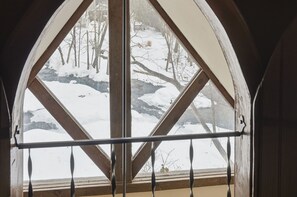 A view through a window with a wooden frame and a metal railing, overlooking a snowy landscape with bare trees and a small stream. - Private 10-Acre Creekside Cabin—80-Ft Deck, Fire Pit, Wildlife & Cozy Spaces! (Canadensis)