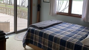 Ett sovrum med en säng, ett fönster med gardiner, en tavla på väggen och utsikt över en terrass och träd utanför.