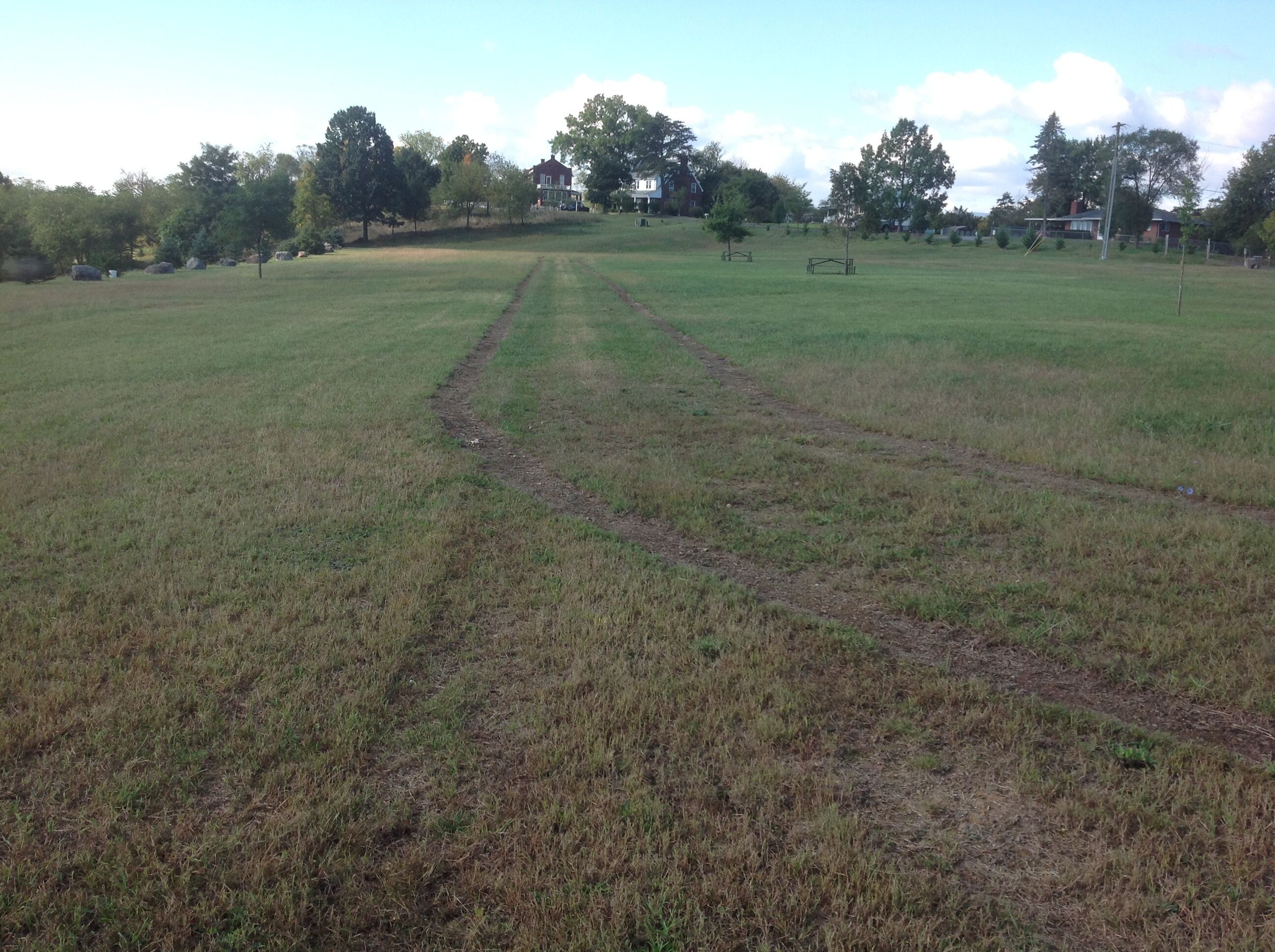 A large open field with a dirt path leading to a distant building.