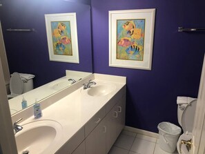 A bathroom with two sinks, a large mirror, and two framed fish paintings on the wall.